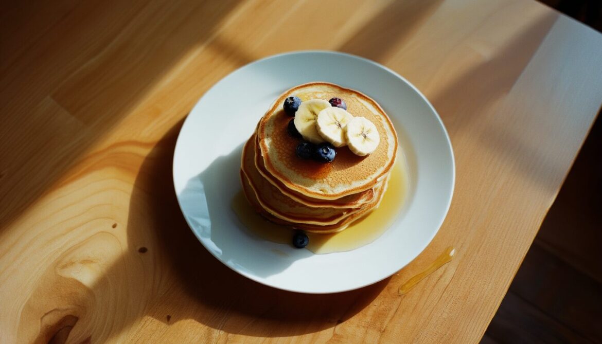 Stapel goldbrauner Bananenpancakes mit Bananenscheiben und Blaubeeren auf einem weißen Teller