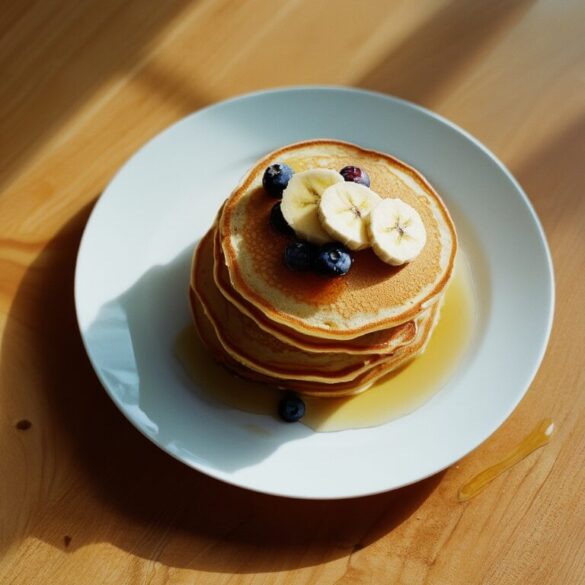 Stapel goldbrauner Bananenpancakes mit Bananenscheiben und Blaubeeren auf einem weißen Teller