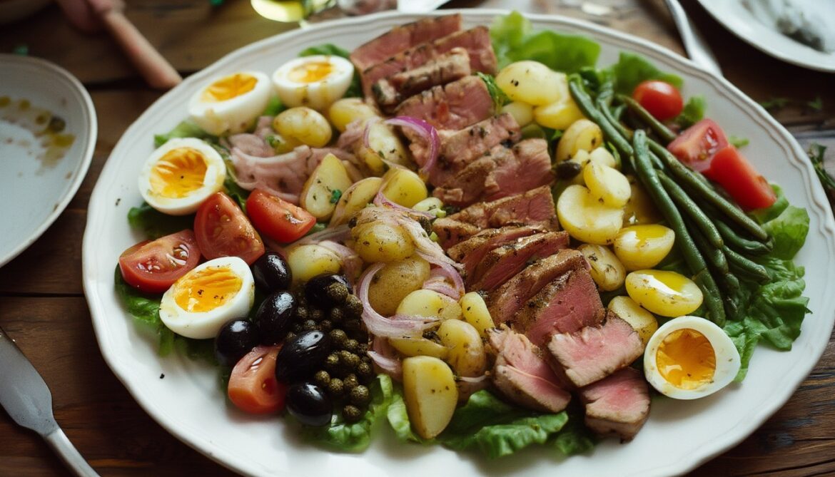 Klassische Salade Niçoise mit Thunfisch, Ei, Kartoffeln, Bohnen, Tomaten und Oliven auf einer weißen Platte angerichtet