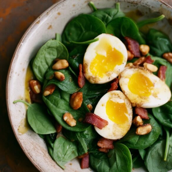 Warmer Spinatsalat mit Ei und knusprigem Speck Warmer Spinatsalat mit knusprigen Speckwürfeln und halbierten Eiern in einer rustikalen Schüssel